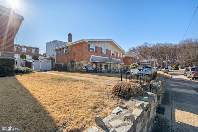 back of property with brick siding, fence, a lawn, a chimney, and a gate