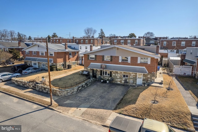 view of front of house featuring brick siding, fence, a residential view, stone siding, and driveway