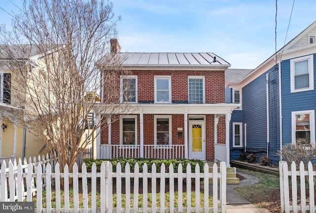 view of front of property with a standing seam roof, a porch, a fenced front yard, brick siding, and metal roof