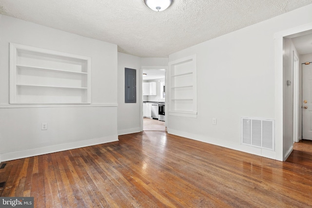 spare room with visible vents, built in shelves, electric panel, a textured ceiling, and wood-type flooring