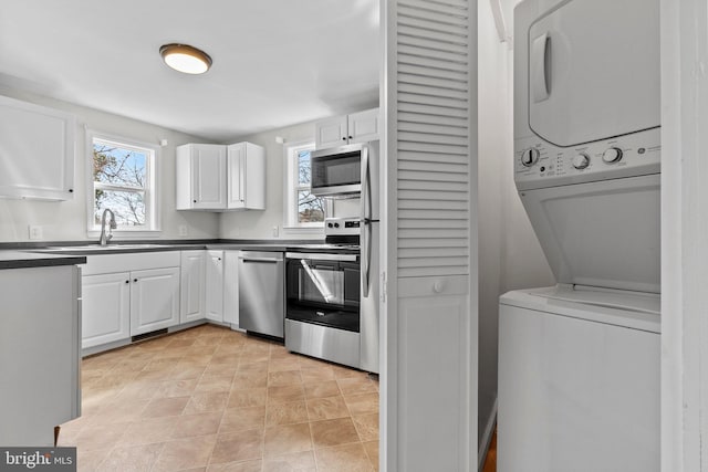 kitchen featuring dark countertops, stacked washer / dryer, white cabinetry, and stainless steel appliances