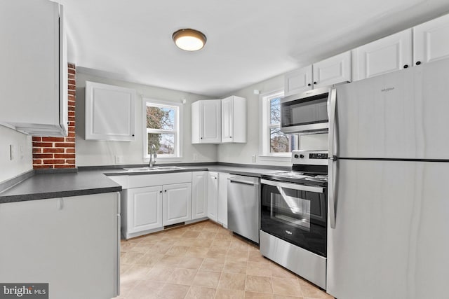 kitchen with a sink, stainless steel appliances, dark countertops, and white cabinetry