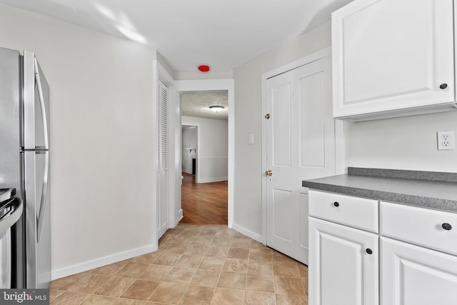 kitchen with baseboards, dark countertops, white cabinets, and freestanding refrigerator