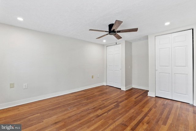 unfurnished bedroom featuring recessed lighting, baseboards, multiple closets, and wood finished floors