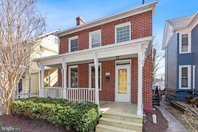 american foursquare style home featuring brick siding, covered porch, and a chimney