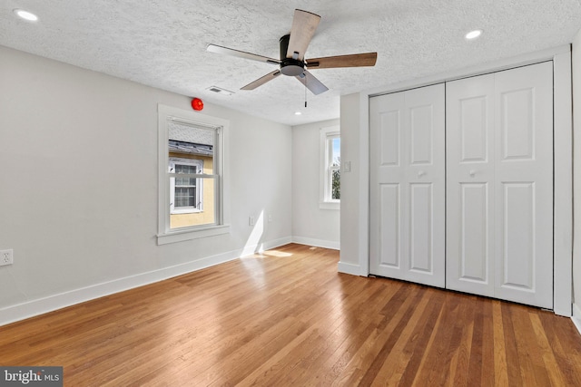 unfurnished bedroom featuring hardwood / wood-style flooring, multiple windows, visible vents, and baseboards