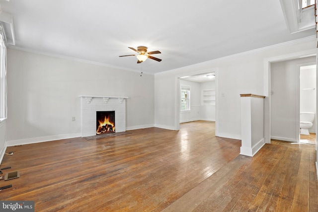 unfurnished living room featuring a ceiling fan, baseboards, a fireplace, ornamental molding, and wood-type flooring