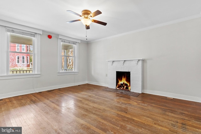 unfurnished living room with a ceiling fan, baseboards, ornamental molding, wood-type flooring, and a brick fireplace