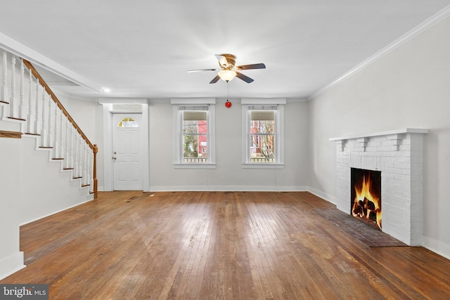 unfurnished living room featuring a brick fireplace, baseboards, stairs, ornamental molding, and wood-type flooring