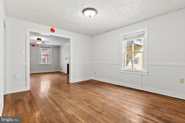 unfurnished room with visible vents, hardwood / wood-style flooring, a textured ceiling, a fireplace, and baseboards