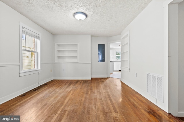 unfurnished room featuring visible vents, wood-type flooring, baseboards, and built in features