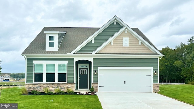 craftsman-style home featuring a front lawn, concrete driveway, roof with shingles, stone siding, and an attached garage