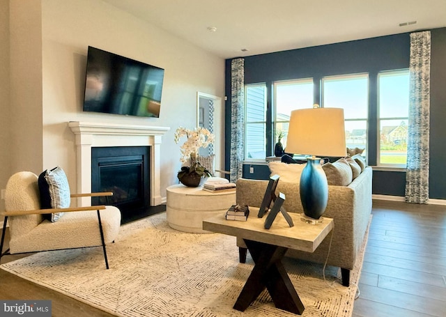 living area with a wealth of natural light, baseboards, wood-type flooring, and a glass covered fireplace