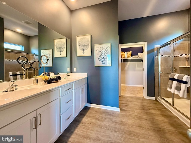 bathroom featuring a shower stall, wood finished floors, double vanity, and a sink