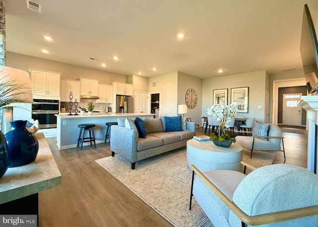 living room with a fireplace, recessed lighting, wood finished floors, and visible vents