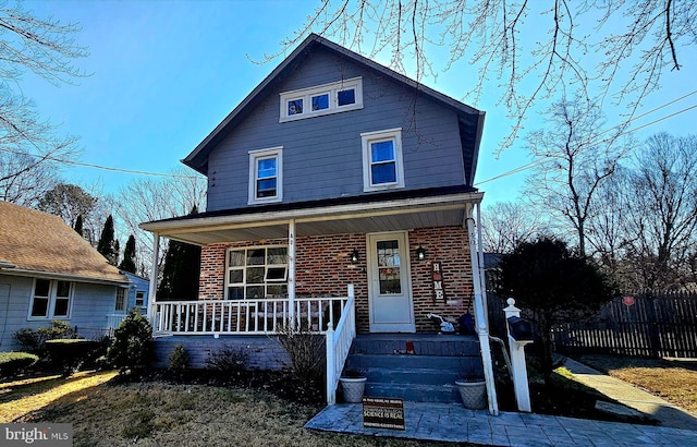 american foursquare style home featuring brick siding, a porch, and fence