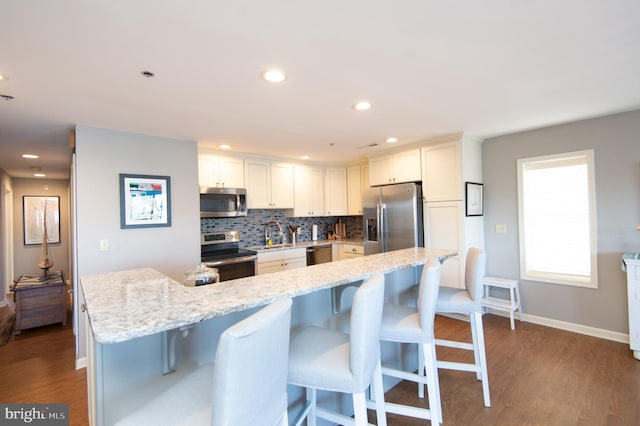 kitchen with decorative backsplash, a kitchen breakfast bar, wood finished floors, and appliances with stainless steel finishes