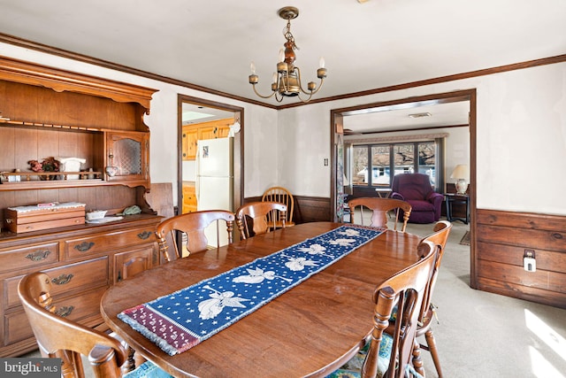 dining space featuring a chandelier, carpet flooring, wainscoting, and ornamental molding