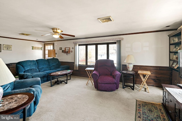 carpeted living room featuring wooden walls, visible vents, a wainscoted wall, and ornamental molding