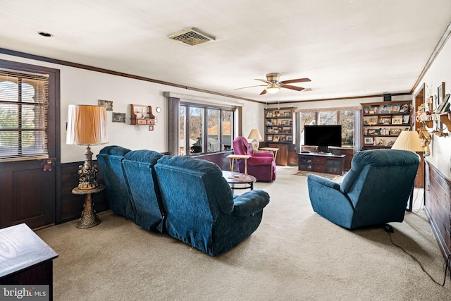 carpeted living area featuring visible vents, a wainscoted wall, a ceiling fan, wood walls, and crown molding