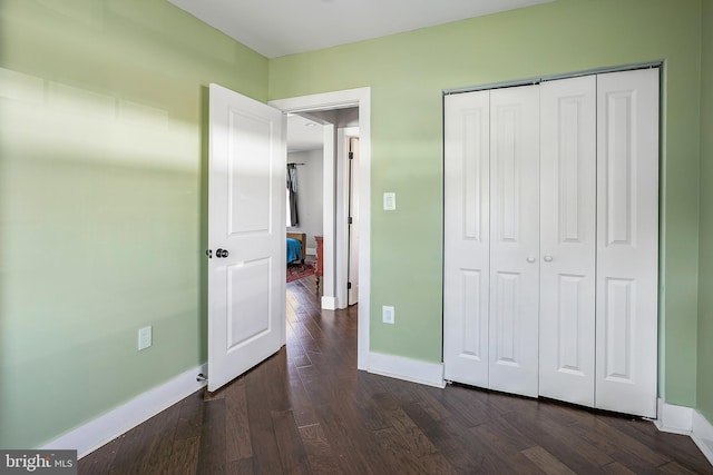 unfurnished bedroom featuring dark wood finished floors, baseboards, and a closet