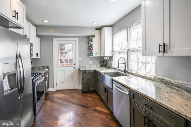 kitchen with light stone countertops, dark wood-style flooring, a sink, appliances with stainless steel finishes, and a wealth of natural light