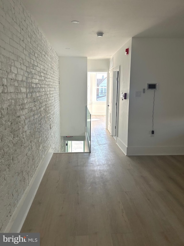 hallway featuring baseboards, wood finished floors, and brick wall