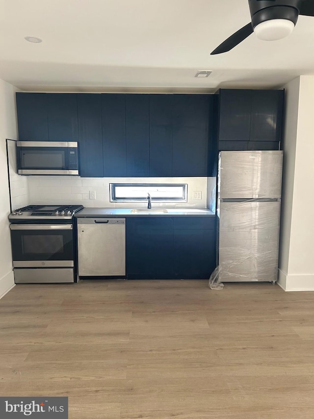 kitchen featuring visible vents, light wood-type flooring, stainless steel appliances, blue cabinets, and a sink