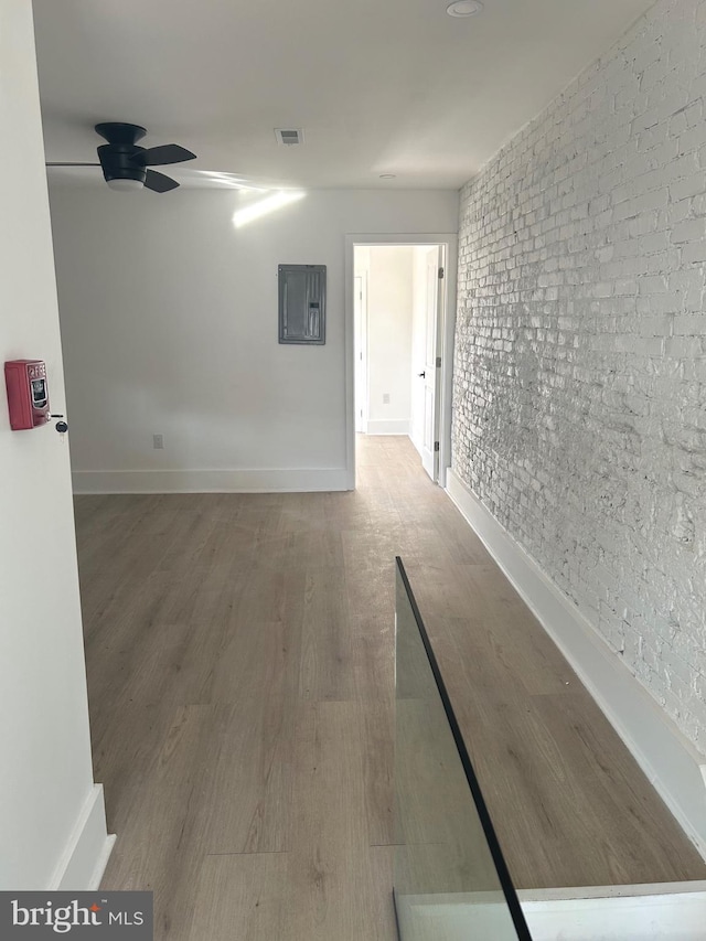 empty room with wood finished floors, visible vents, brick wall, baseboards, and electric panel