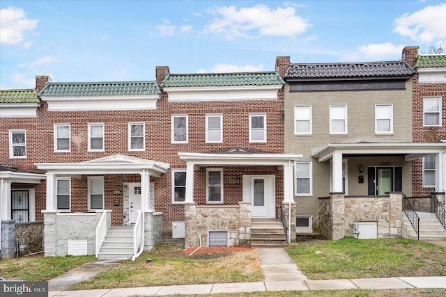 multi unit property with a tiled roof, mansard roof, covered porch, and brick siding