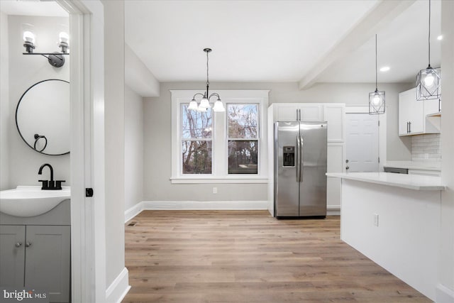 kitchen with light wood-type flooring, light countertops, beam ceiling, stainless steel refrigerator with ice dispenser, and a sink