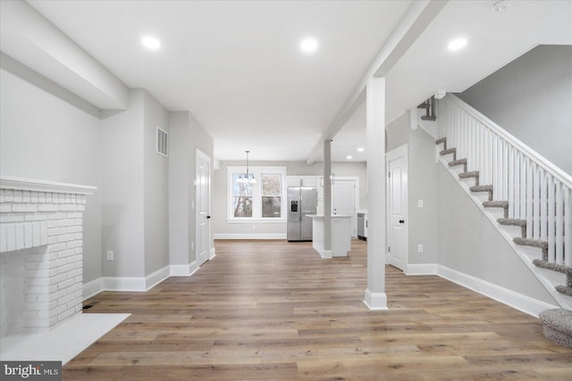 unfurnished living room with stairway, a brick fireplace, and wood finished floors