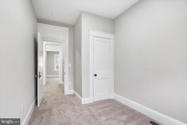 hallway featuring light colored carpet and baseboards