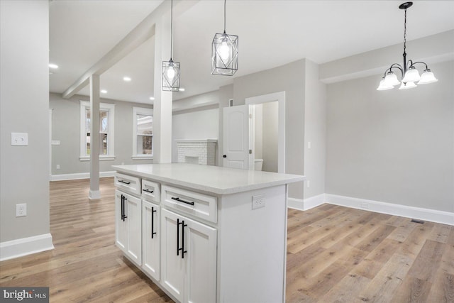 kitchen featuring light wood-type flooring, decorative light fixtures, a center island, white cabinetry, and baseboards