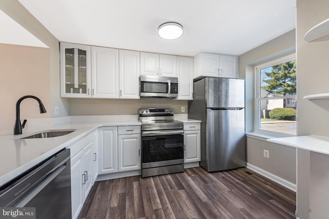 kitchen featuring dark wood-style flooring, appliances with stainless steel finishes, glass insert cabinets, and a sink