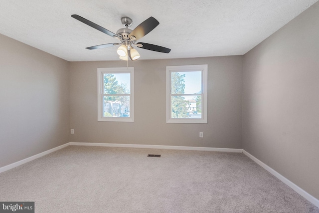 carpeted spare room with visible vents, baseboards, a textured ceiling, and a ceiling fan