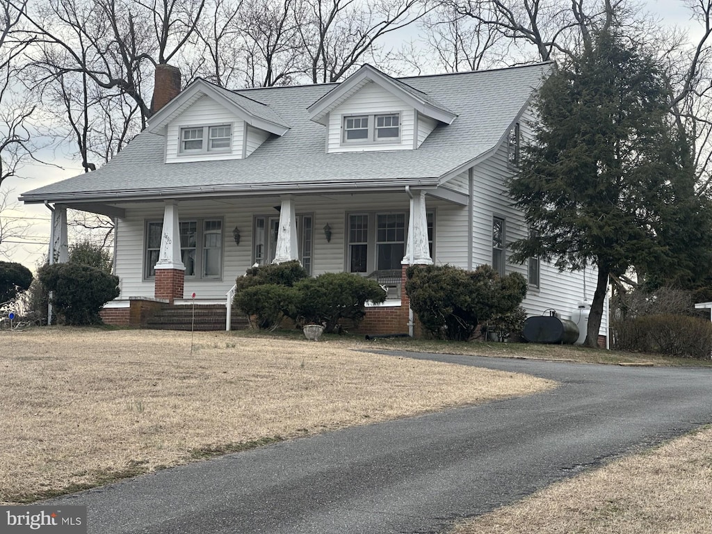 view of front of property featuring a front yard, roof with shingles, covered porch, a chimney, and heating fuel