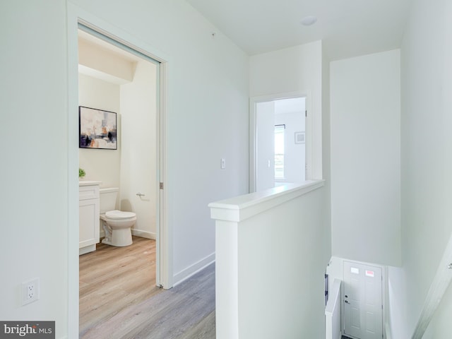 hall with baseboards, an upstairs landing, and light wood-style floors