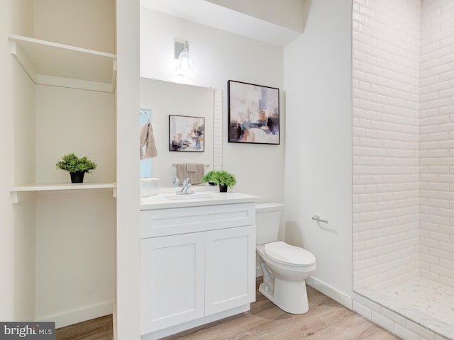 bathroom featuring a tile shower, toilet, vanity, and wood finished floors