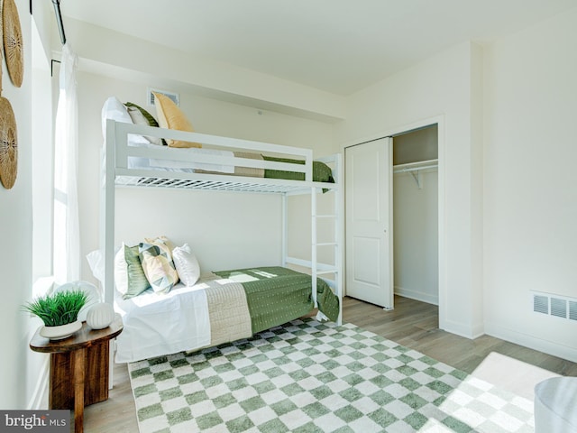 bedroom with a closet, visible vents, baseboards, and wood finished floors