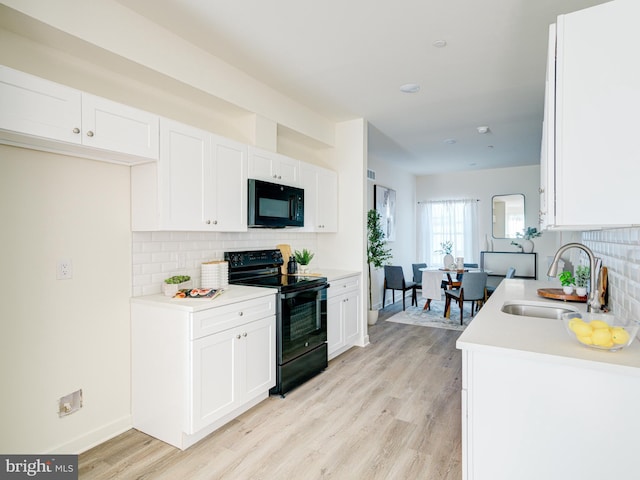 kitchen with light wood-style flooring, a sink, black appliances, light countertops, and white cabinetry