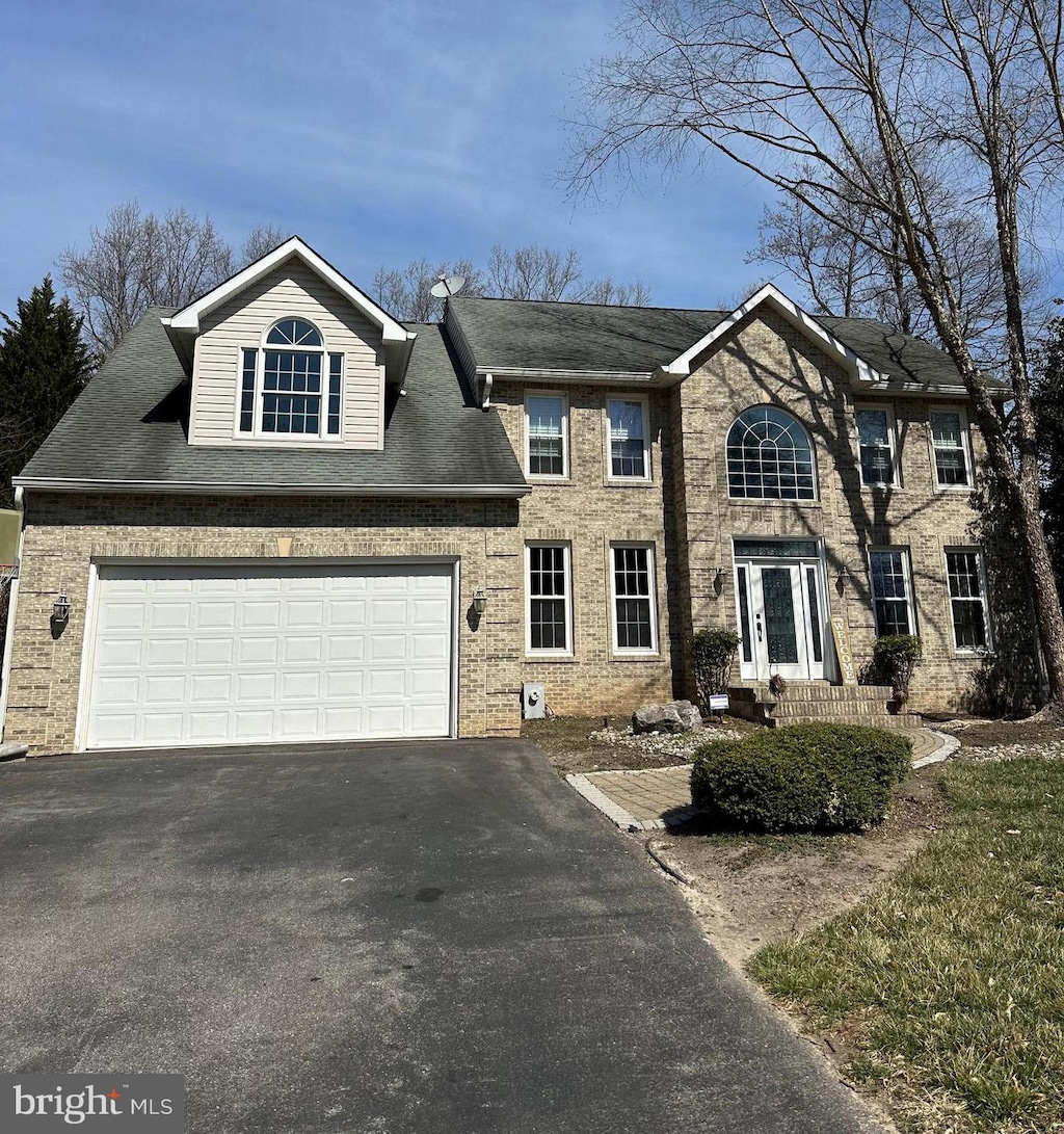 colonial inspired home featuring aphalt driveway, a garage, brick siding, and a shingled roof