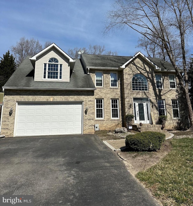 colonial inspired home featuring aphalt driveway, a garage, brick siding, and a shingled roof