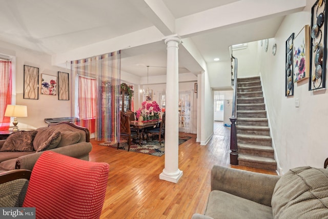 living area with decorative columns, a notable chandelier, stairway, and light wood finished floors