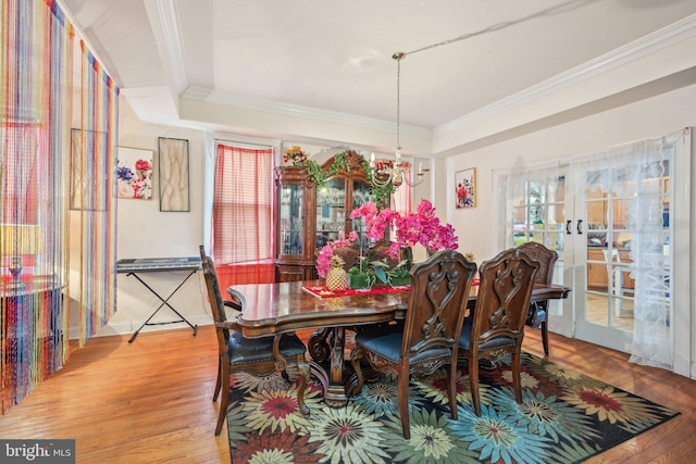 dining room featuring light wood-type flooring, an inviting chandelier, crown molding, and french doors