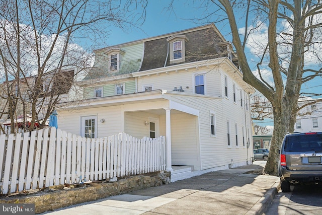 victorian home with mansard roof, roof with shingles, and fence