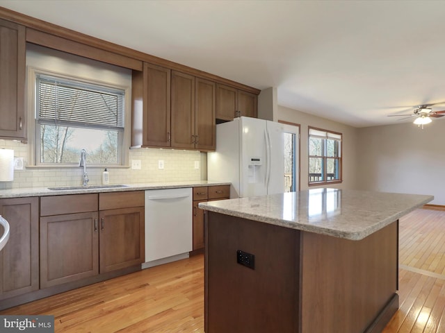 kitchen featuring white appliances, a kitchen island, light wood-style flooring, a sink, and backsplash