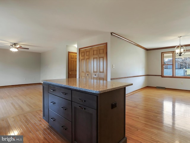 kitchen with light wood-type flooring, ceiling fan with notable chandelier, a kitchen island, baseboards, and light stone countertops