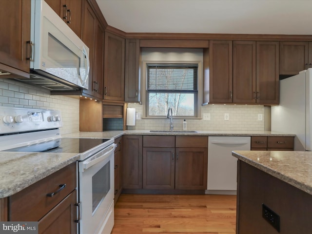 kitchen with a sink, backsplash, white appliances, light wood finished floors, and light stone countertops