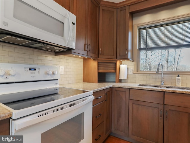 kitchen featuring a sink, white appliances, tasteful backsplash, and light stone counters